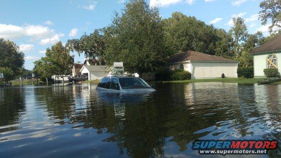 Silver minivan partially submerged in floodwaters, with a ladder on its roof