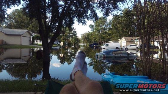 Flooded street with cars submerged in water, seen from a person relaxing in a chair with their feet up