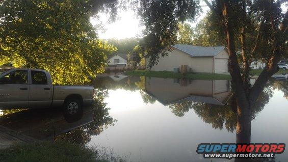 Silver pickup truck parked on a flooded street, houses and trees reflected in the water