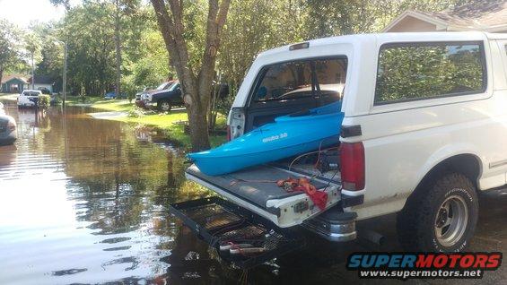 White SUV with a blue kayak in the cargo area, parked in flooded street