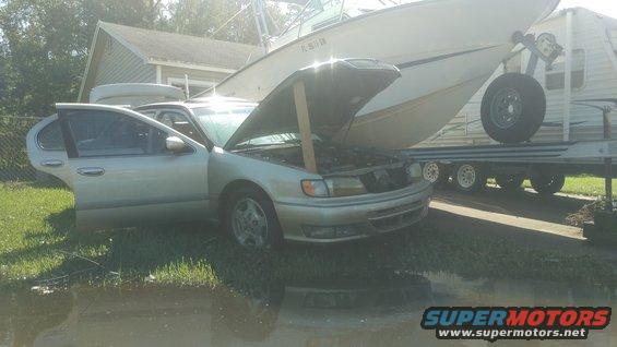 Silver sedan with hood propped open, parked on grass. A boat on a trailer is behind it