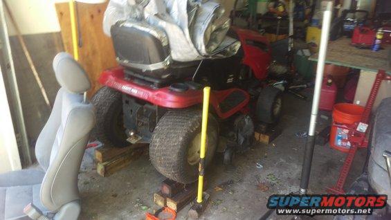 Red riding mower on wooden blocks in a garage. A car seat is in the foreground