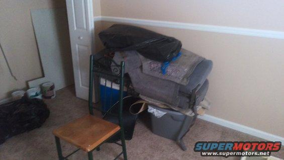 Stacked items including a black trash bag, fabric, and a plastic bin in a room with a chair