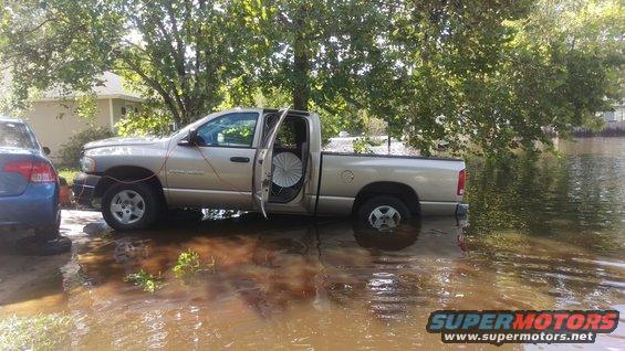 Side view of a tan pickup truck partially submerged in floodwater, with doors open