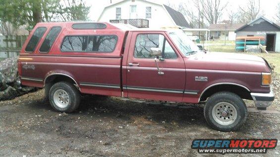 Maroon Ford F-150 pickup with a red camper shell parked on a dirt lot