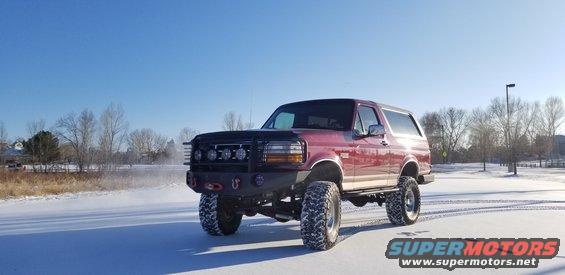 Red Ford Bronco with aftermarket bumper and lights on snowy ground