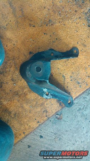 metal bracket with holes, sitting on a textured surface. Supermotors.net logo visible