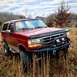 1995 Ford Bronco - This red Ford Bronco is equipped with a winch and aftermarket bumper, parked in a field under power lines.