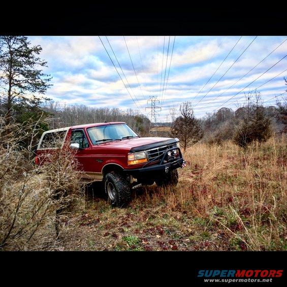 Red 1995 Ford Bronco with winch and aftermarket bumper parked in a field