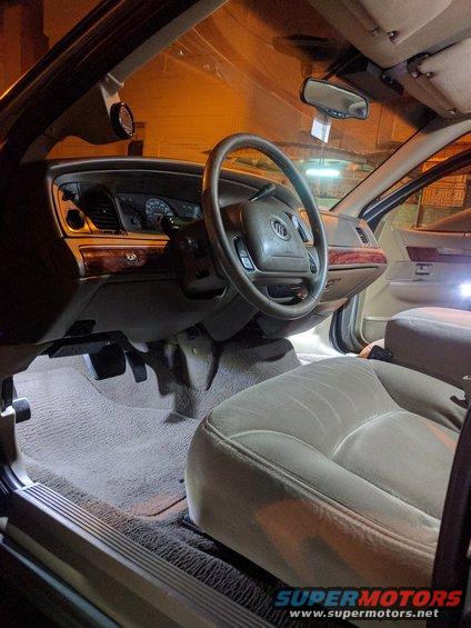 2001 Mercury Grand Marquis interior with tan leather seats, wood trim, and dashboard. LED lights illuminate the floor