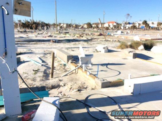 Debris-strewn landscape with damaged buildings and vegetation under a clear blue sky