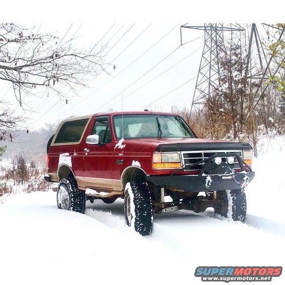 Red 1995 Ford Bronco with aftermarket bumper and off-road tires in snow