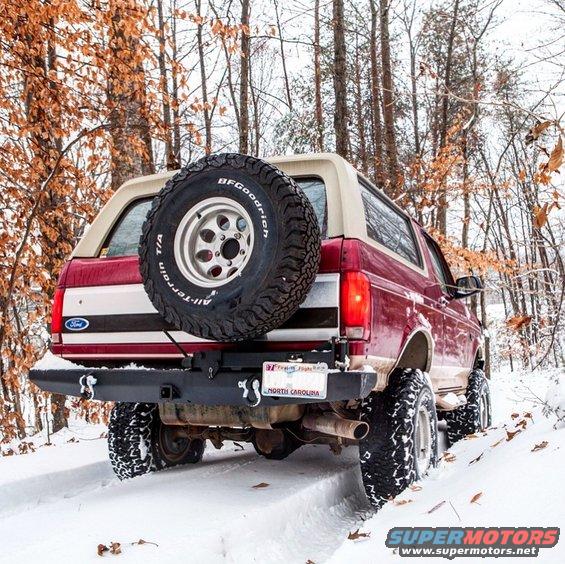 Red 1995 Ford Bronco with spare tire on back driving in snow through trees