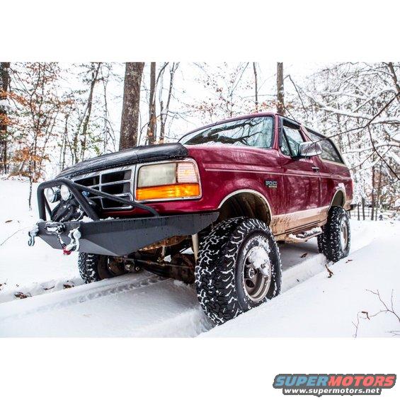 Red Ford Bronco with aftermarket bumper and large tires driving in snow