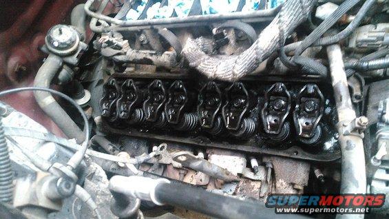 Close-up of an engine's valve train with rocker arms visible. Some hoses and wiring are also in the shot