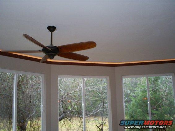 Ceiling fan with wooden blades above windows overlooking trees