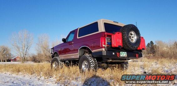 Maroon Ford Bronco with tan top, lifted suspension, and spare tire mounted on rear bumper with two red jerry cans