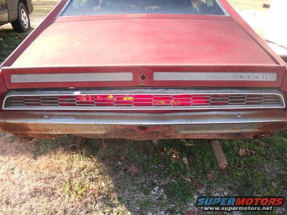 Red 1970 Ford Torino rear end with chrome bumper and horizontal taillights. A dark SUV is partially visible on the left