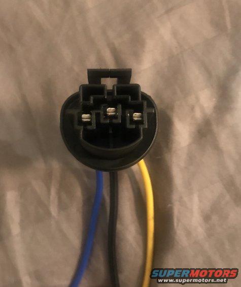 Close-up of a black electrical connector with three metal pins and three colored wires (blue, black, yellow) attached