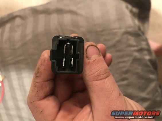 Close-up of a black electrical connector with four metal pins, held by a dirty hand