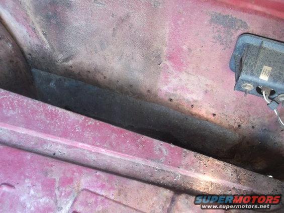 Close-up of a red car's interior panel with some rust and a black electrical component labeled 'RH'