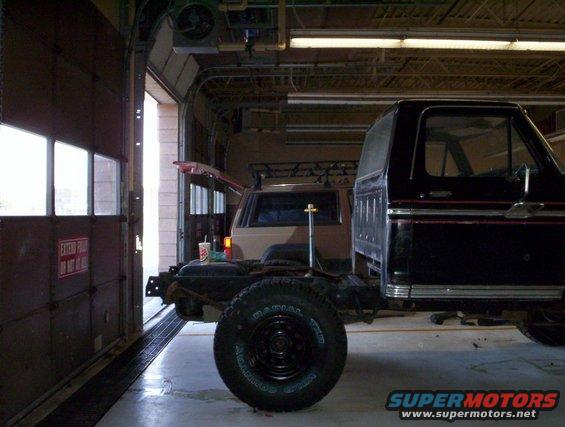 Black Ford Bronco body on a chassis, another SUV behind it in a garage