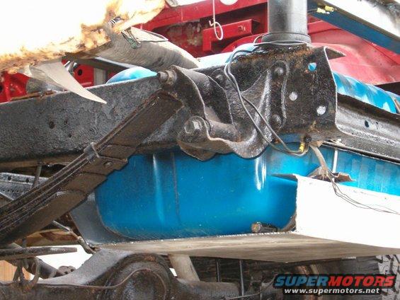 Close-up of vehicle underbody showing leaf springs, black frame components, and a bright blue fuel tank
