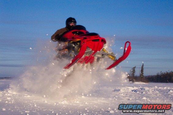 Snowmobile airborne over snow, rider wearing helmet and jacket