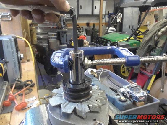 Socket wrench turning bolt on alternator pulley held by C-clamp