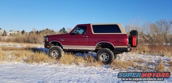 Red 1996 Ford Bronco with a tan removable top, lifted suspension, and a spare tire mounted on the rear tailgate