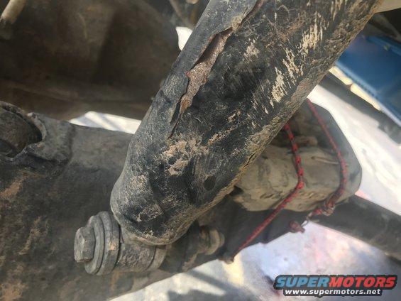 Close-up of a damaged black shock absorber with rust showing through cracks and a red rope tied around it