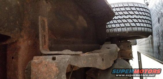 Underside of a rusty vehicle frame with a tire visible.