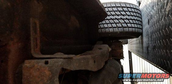 Underside of a vehicle showing rusted metal frame and a tire against diamond plate.