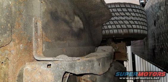 Underside of a vehicle with heavy rust on frame and body panels, tire visible.