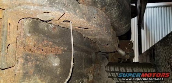 Underside of a vehicle frame with heavy rust and a hanging wire.