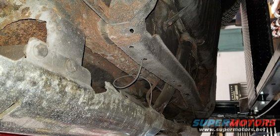Underside of a vehicle showing rusty frame and suspension parts.
