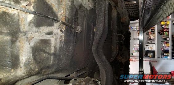Underside of a vehicle chassis with exhaust pipes and brake cable.
