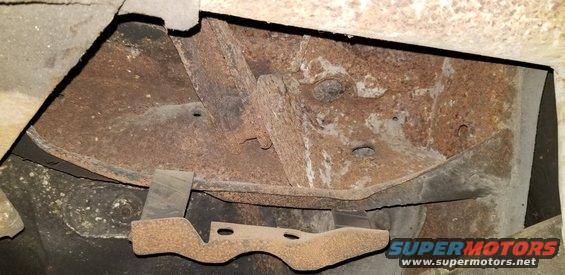 Underside of a vehicle showing rusted frame and a metal bracket.