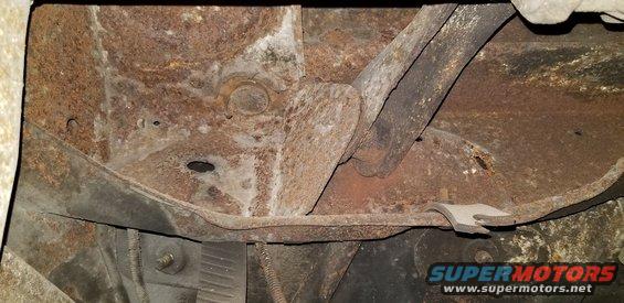 Underside of a vehicle chassis with heavy rust on frame and suspension parts.