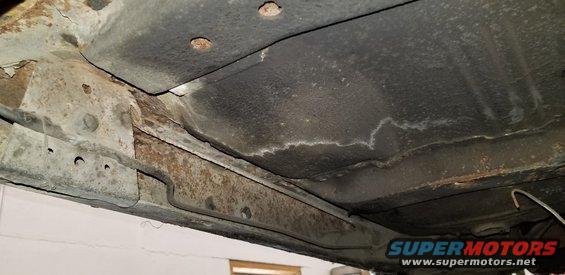 Underside of a car showing rusted frame rails and brake line.
