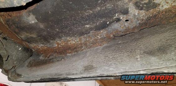 Underside of a vehicle with extensive rust and a crack in the metal.