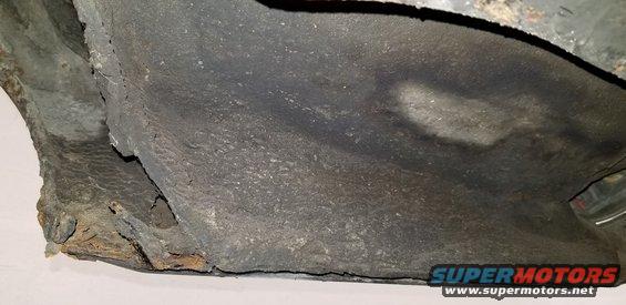 Underside of a vehicle with rust and peeling undercoating.