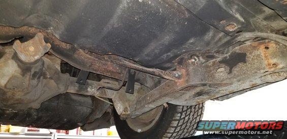 Underside of a vintage car showing rusted differential, exhaust, and suspension parts.