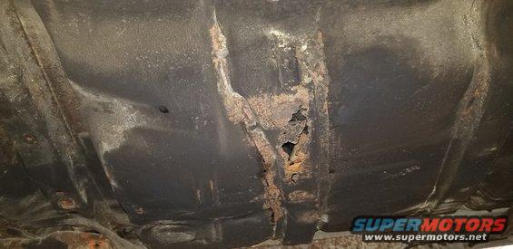 Undercarriage of a car with severe rust and holes in the frame.