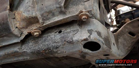 Underside of a rusty vehicle frame with bolts.
