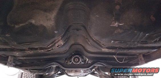 Underside of a classic car chassis, showing the transmission tunnel and exhaust.