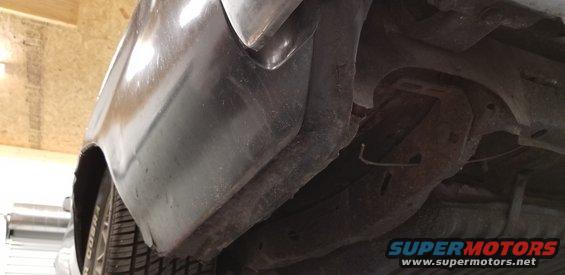 Undercarriage of a vehicle showing rear fender well and suspension components with visible rust.
