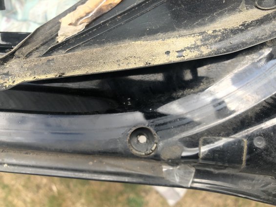 Close-up of a black car hatch with a mounting hole and some dirt. Shows a plastic trim piece