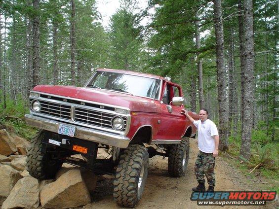 Red lifted Ford pickup truck with large tires on a rocky trail, a man stands beside it