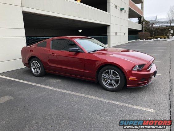 Red 2014 Ford Mustang coupe parked in a lot next to a parking garage